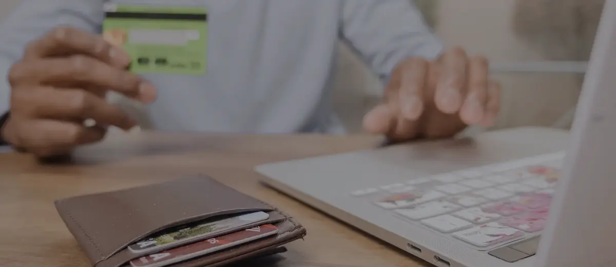 A person holding a green credit card at a desk with a laptop.