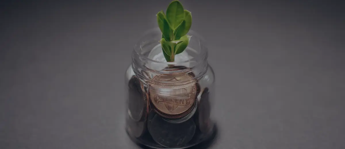 A small plant sprouting from a jar of coins against a dark background.