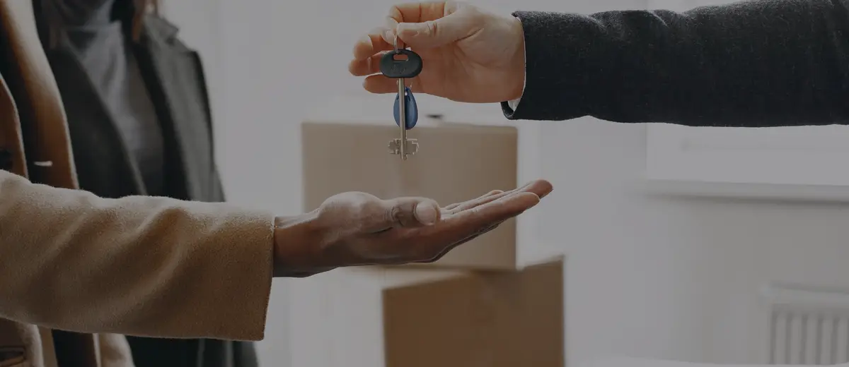 Apartment keys being handed over, with moving boxes behind.