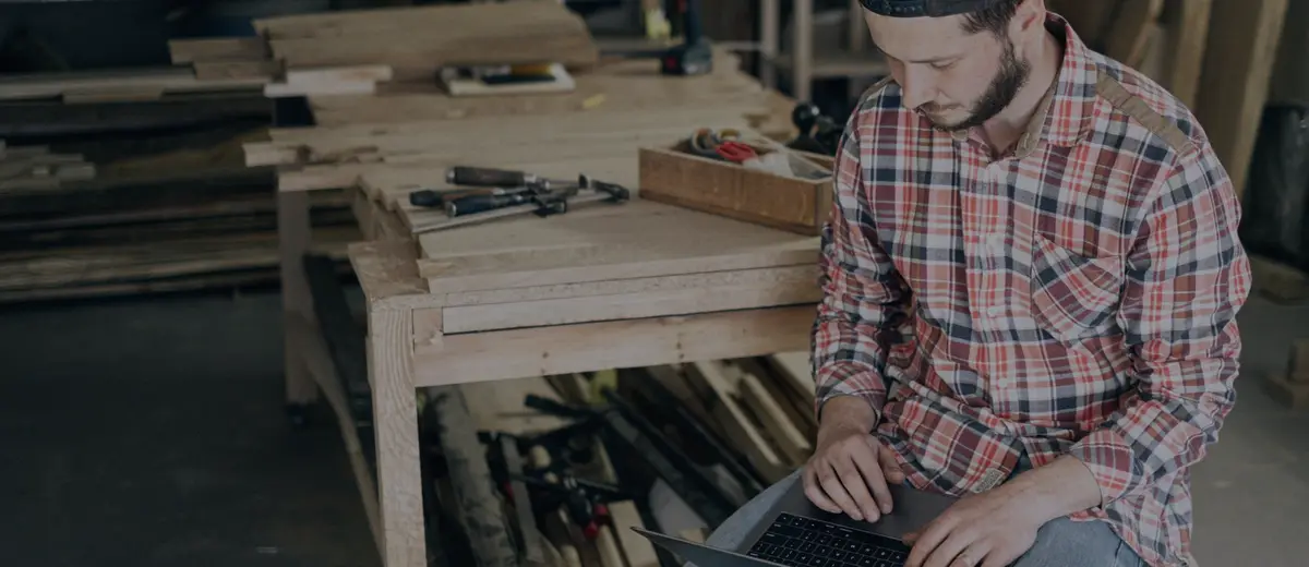A woodworker using a laptop in his workshop.