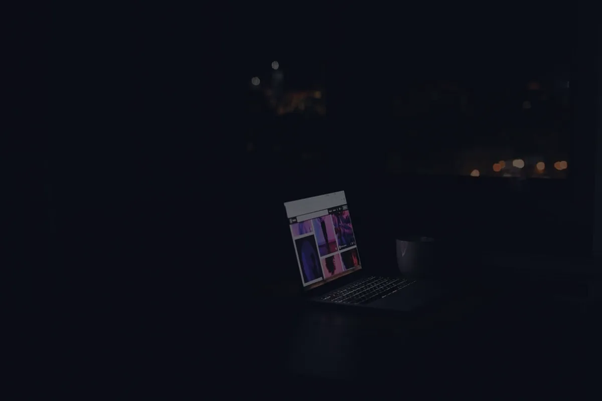 A laptop glowing at night in a dark room, representing starting a side hustle.
