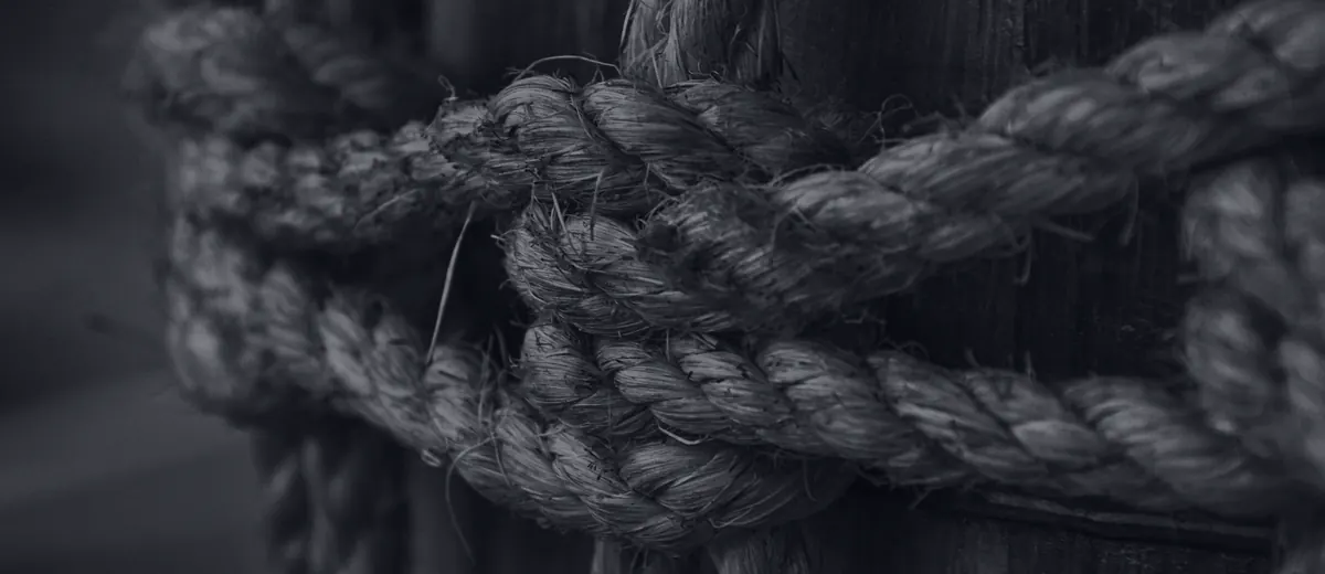A black-and-white close-up of thick rope knotted around a wooden post.