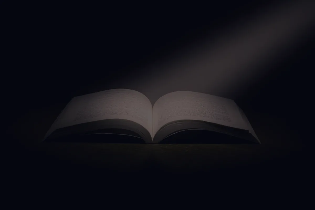 An open book in a beam of light on dark, representing student loan forgiveness.