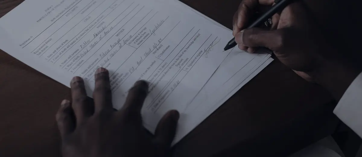 Hands signing a document with a pen on a dark wooden desk.