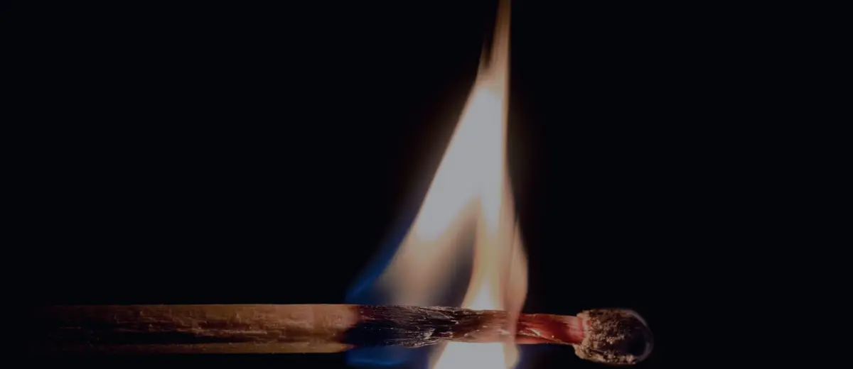 A single matchstick bursting into flame against a black background.