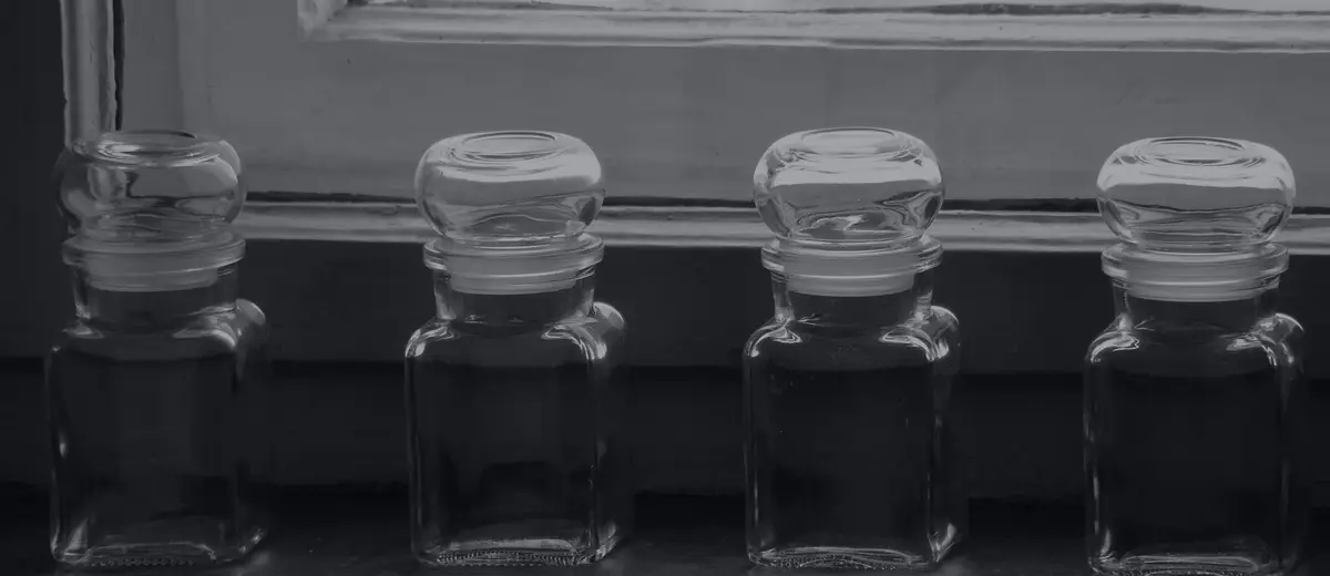 Four empty glass jars lined up on a windowsill, in black and white.