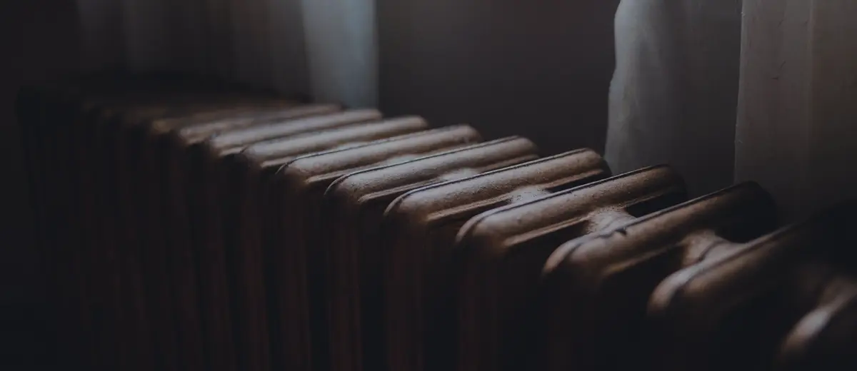 A radiator under a window with a sheer curtain.