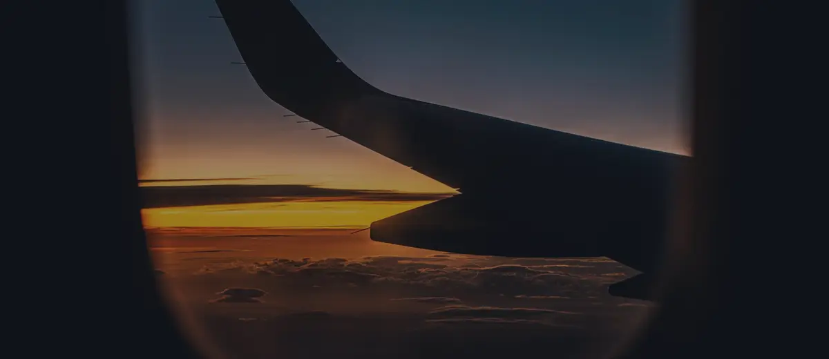 An airplane wing seen through a window at sunset.