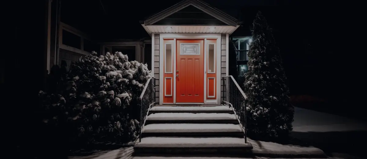 A lit red front door and steps of a house at night.